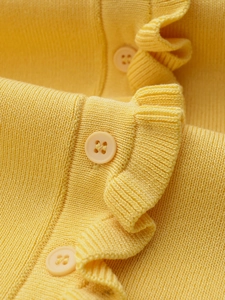 Detail of yellow knit top featuring wavy ruffle edges and matte round buttons