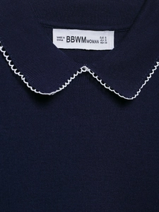 Détail du haut en tricot bleu marine avec col en V, bordure festonnée blanche et étiquette