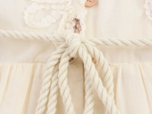 Detail of crochet lace trim with wooden buttons and natural cotton rope belt on beige dress