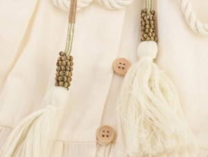 Detail of bohemian cream dress with wooden buttons, braided ropes and beaded tassels