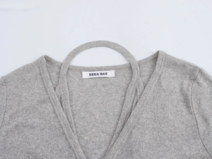 Dettaglio top in maglia grigia con scollo a V, anello halter e chiusura a bottoni singoli