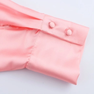Détail du poignet d'une chemise en satin rose avec deux boutons recouverts de tissu