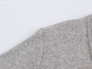 Dettaglio della cucitura della spalla su una maglia grigia a maniche lunghe con scollo a V