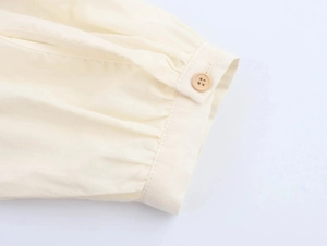 Close-up of pleated cuffs and wooden button on beige floral embroidered dress