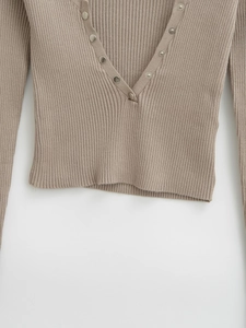 Detailed view of light brown rib-knit fabric with silver snap buttons and V-neckline