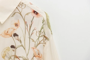 Close-up detail of beige long-sleeve shirt with orange poppy flower print and fine texture