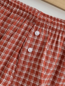 Detail view of elastic waistband and decorative white buttons on red plaid shorts