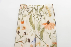 Detail view of high waist trousers with floral watercolor print and brown piping trim