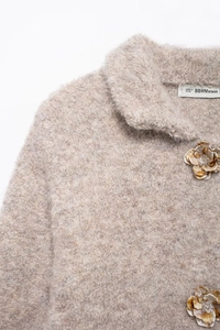 Dettaglio ravvicinato di cardigan in maglia beige con bottoni floreali e trama in pelliccia