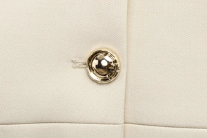 Gros plan sur le tissu sergé beige clair et le bouton décoratif en métal doré