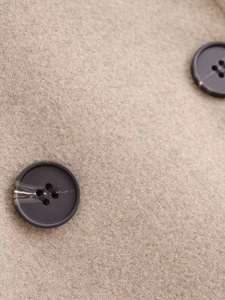 Gros plan sur le tissu beige d'une veste en laine et ses boutons gris marbrés
