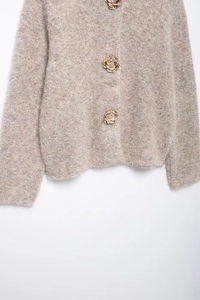 Dettaglio del cardigan in maglia marrone chiaro con bottoni floreali 3D e consistenza soffice