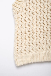 Détail de gilet en tricot crème montrant la maille épaisse et les bords côtelés