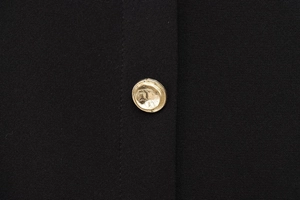 Détail d'un bouton en métal doré martelé sur le tissu d'une robe midi noire
