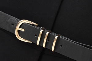 Détail macro d'une ceinture en cuir noir avec boucle ardillon dorée et trois passants