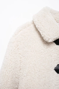 Detailed close-up of white sherpa fabric texture with black buckle on a short jacket