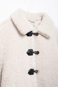 Close-up of ivory teddy coat featuring premium leather buckles and gold metal buttons