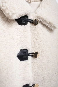 Detailed close-up of cream faux fur texture with faux leather and gold horn button