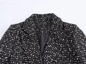 Close-up of black and white tweed blazer texture showing woven fabric and inner collar tag