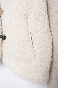 Close-up of cream faux shearling jacket fabric with pocket detail and gold metal button