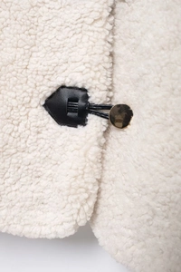 Detail of white faux shearling jacket with black leather trim and gold metal fastener