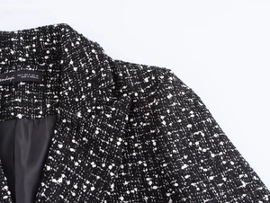 Detail view of black and white tweed blazer shoulder with woven size label and fabric texture