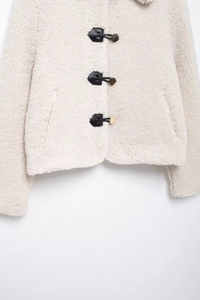 Detail of white sherpa fleece jacket with black leather trim and golden metal buttons