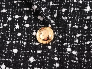 Detail of black and white tweed fabric with a vintage golden textured metal button
