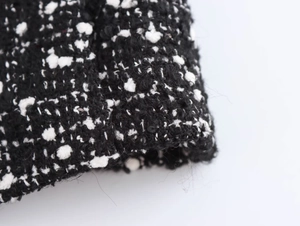Macro shot of textured black and white tweed fabric on women's cropped blazer