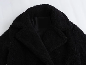 Detail of a black faux lamb wool coat featuring a wide notched lapel and thick texture