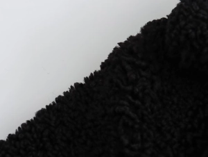 Close-up of thick black sherpa fleece fabric showing curled granular texture on a coat