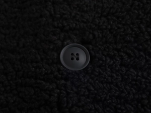 Close-up of matte black button and textured fleece fabric on a long winter coat