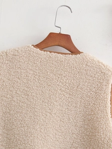 Close-up of off-white sherpa fleece vest featuring contrast brown leather piping detail