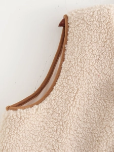 Close-up of beige sherpa fleece vest with brown suede piping and thick texture detail