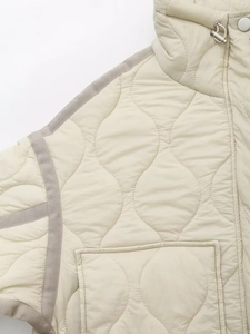 Détail du matelassage ondulé sur une veste beige avec cordon argenté et ruban gris