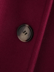 Detailed macro view of a brown marble button on a thick burgundy wool coat fabric