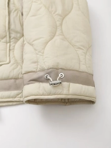 Détail de l'ourlet à cordon ajustable avec œillet métallique sur veste matelassée beige