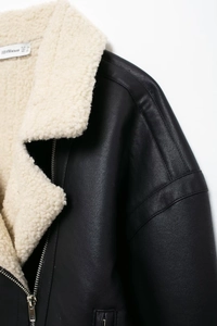 Détail de la veste biker en simili cuir noir avec col en fausse fourrure blanche et zip argenté