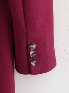 Close-up of wine red wool coat sleeves featuring three marbled button decorations