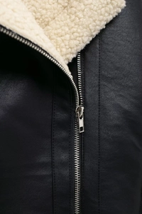 Détail d'une veste en cuir noir avec col en laine beige et fermeture éclair argentée