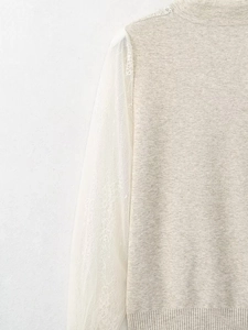 Detailed close-up of textured knit fabric with delicate white lace sleeves on a beige top