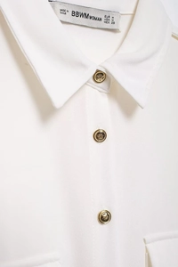 Detail of cream long-sleeved shirt featuring gold embossed buttons and collar texture