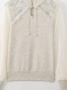 Close-up of beige knit top featuring lace patchwork sleeves and pearl drop pendant