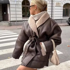 Oversized dark brown faux leather shearling coat with belt worn by a model in city street