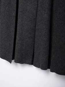 Macro shot of charcoal grey wool blend fabric showing thick texture and neat pleats