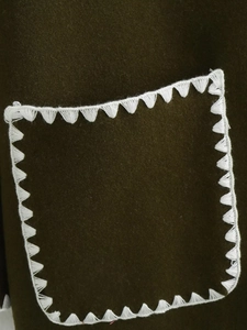 Detail eines olivgrünen Wollmantels mit weißem Dreieck-Stickstich am Taschenrand