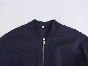 Close-up of navy blue bomber jacket showing ribbed collar, metal zipper, and size S label