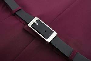 Détail d'une robe plissée bordeaux avec une ceinture en cuir noir et boucle argentée