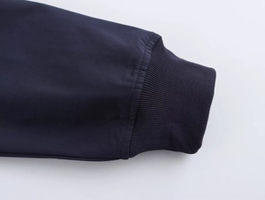 Detailed macro view of the dark blue ribbed cuffs on a street style cropped baseball jacket