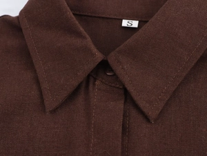Dettaglio macro del colletto della camicia marrone scuro con trama e etichetta taglia S